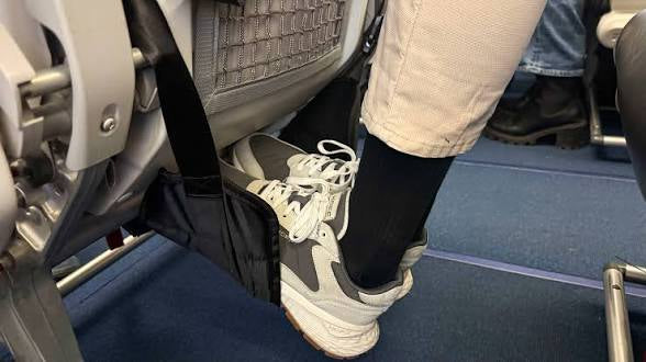 The Packt Hammock portable airplane footrest in Black — front view showing nylon hammock and strap